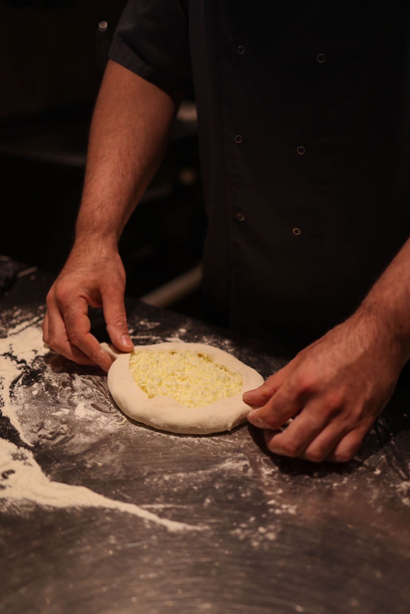 Manos del cocinero estirando la masa sobre la mesa de acero enharinada